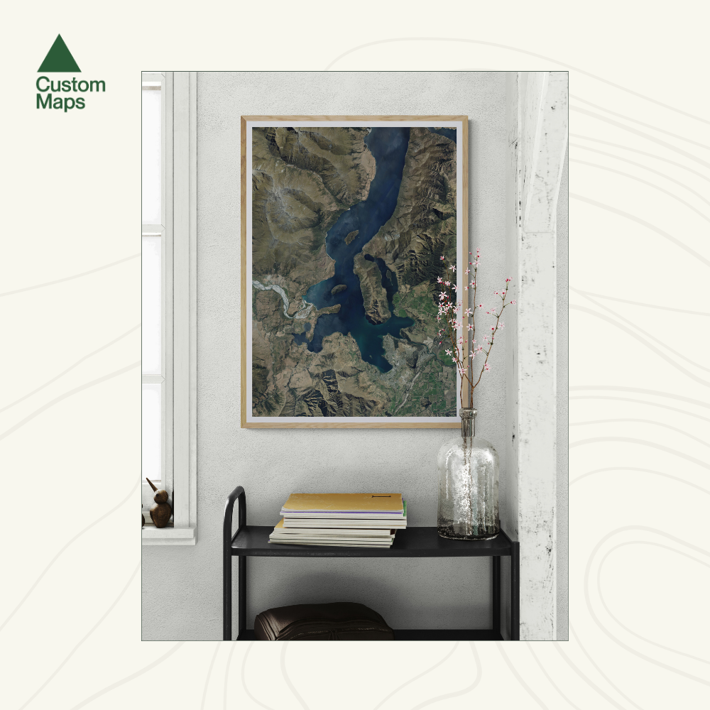Aerial print of Wanaka on a wall above a shelf with books and a vase.