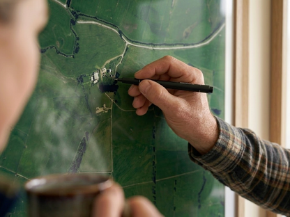 Person holding a pen over a farm map on a glass surface