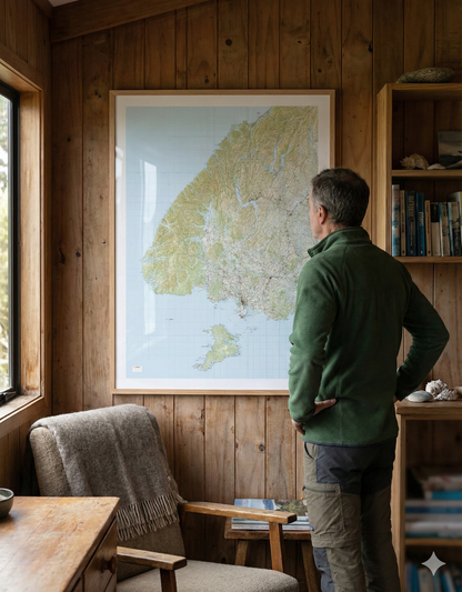 Man standing in a bach looking at a Fiordland map on the wall