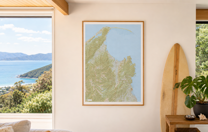 Framed map of Abel Tasman and Golden Bay on a wall with a view of water and trees outside.