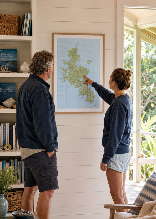 A couple stands in a bright, modern home interior looking at a framed map hanging on the wall of Great Barrier Island