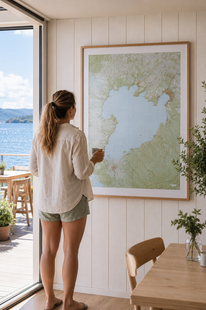 Woman standing by a large framed map of Lake Taupo, looking out at water from a room with wooden floors and a large window.
