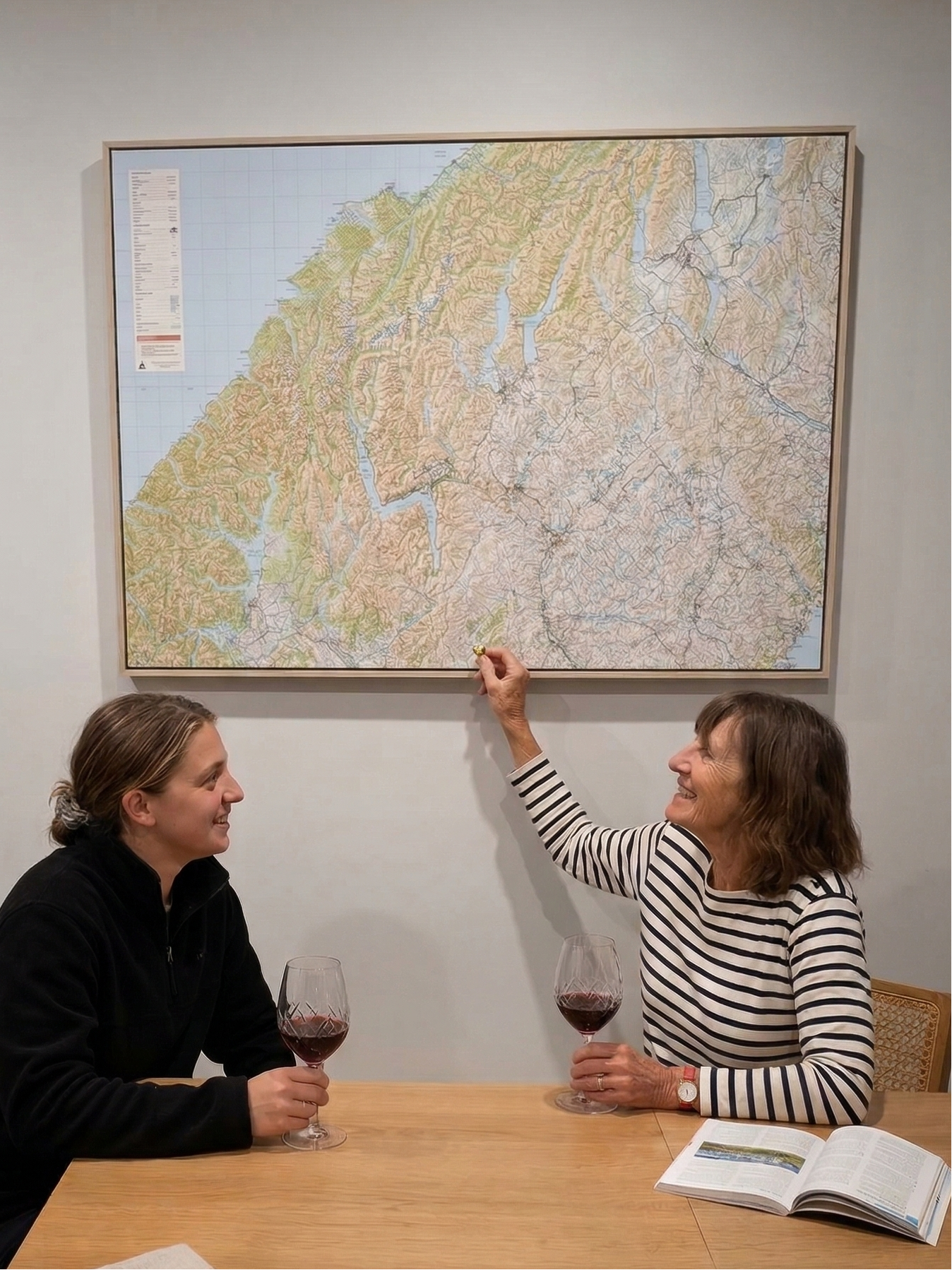 Two people sitting at a table with a map of on the wall, one person pointing to the map.